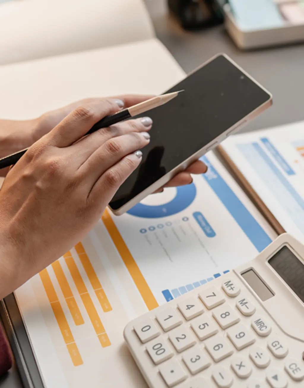 Close-up of a person using a tablet and stylus beside budget charts and a calculator.
