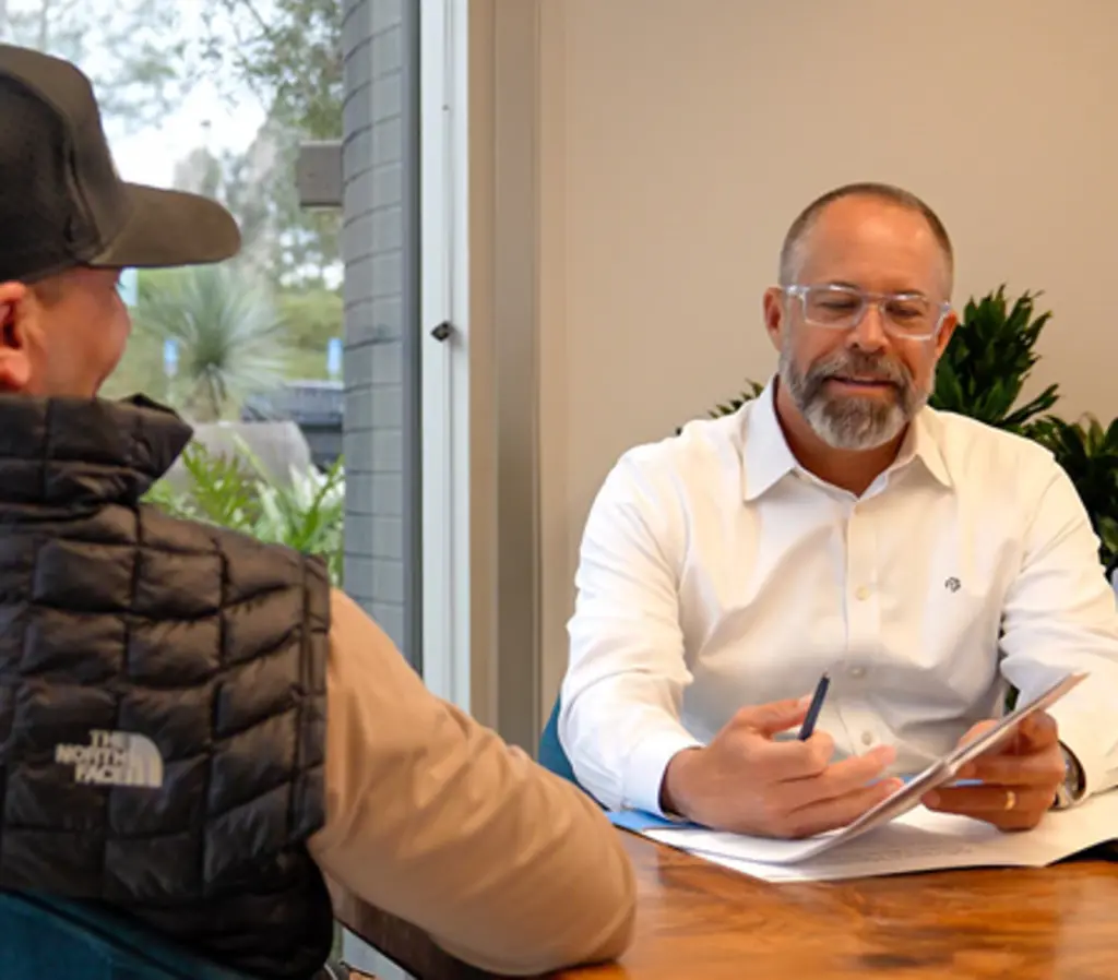 Man reviewing documents with another man at a table.