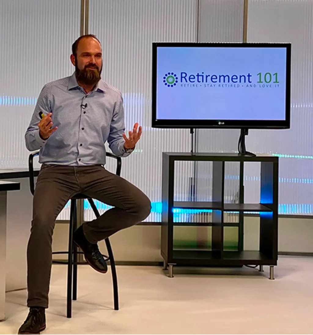 Man speaking during a retirement workshop beside a screen displaying the Retirement 101 logo.