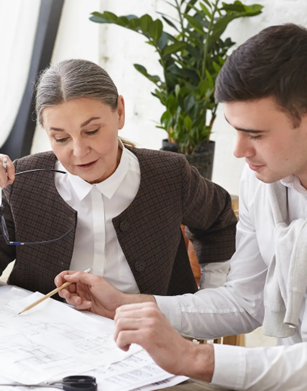 Senior architect and younger colleague reviewing building plans at a desk.