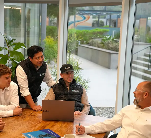 Four colleagues gathered around a table in a modern office, discussing work while looking at a laptop during a collaborative meeting.